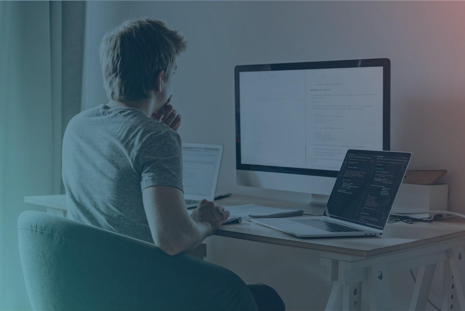 A software developer is programming and reading on two screens.
